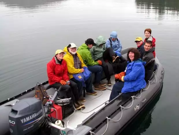 A group of explorers in colorful jackets sit in zodiac in calm waters.