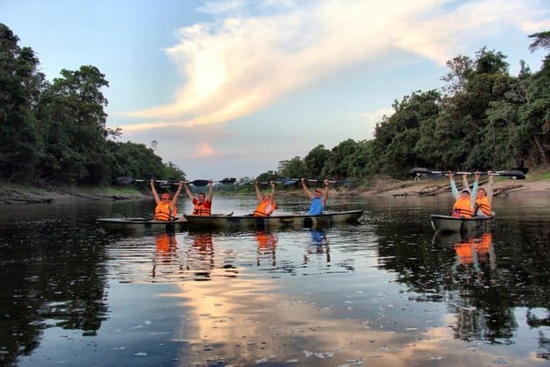 Delfin II travelers are paddling double kayaks wearing life jackets and holding their paddles in the air for celebration. 