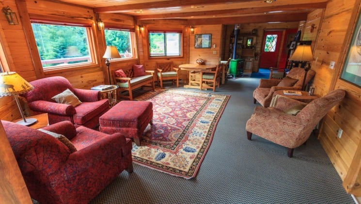 The lounge, with a wood interior, big and comfortable chairs, a rug, and cozy decor, at the Tutka Bay Wilderness Lodge in Alaska