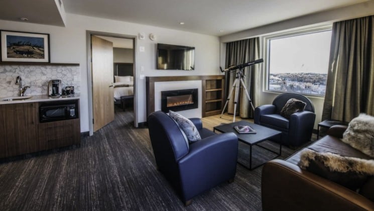 Loveseat, fireplace, two armchairs, coffee table, kitchenette and telescope in Aurora Signature Suite at Explorer Hotel in Yellowknife, Northwest Territories
