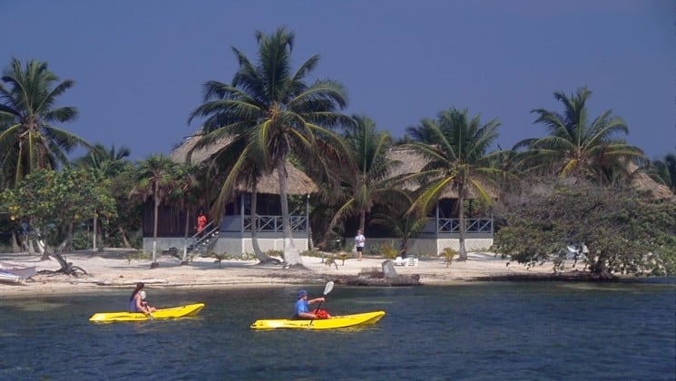 Two kayakers paddle in the ocean, in front of the pristine beach, where the Blackbird Caye Resort in Belize is located