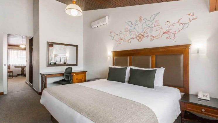 King bed with hand-painted birds on wall, small writing desk and bedside table in king suite at Costa del Sol Ramada Cusco in Peru