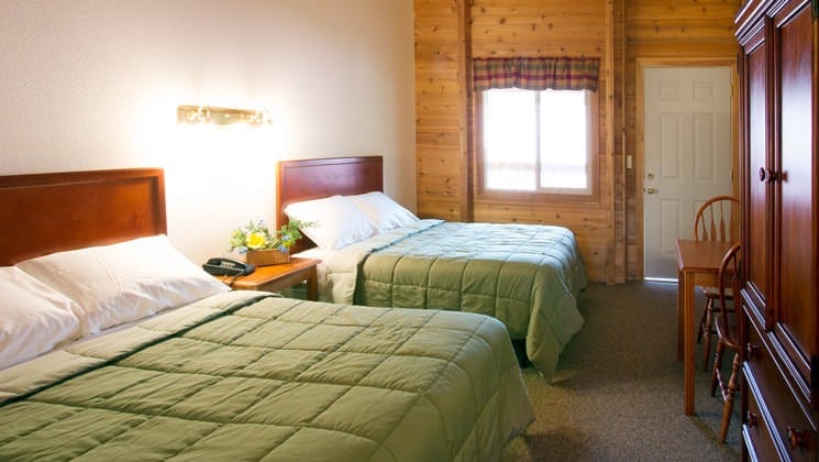 Two queen-sized beds with green down comforters inside one of the guest cabins at Kantishna Roadhouse, an Alaskan lodge in Denali National Park