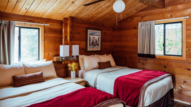 Wood cabin interior with two queen beds, two windows, bedside table and ceiling fan at Denali Backcountry Lodge in Kantishna, Alaska