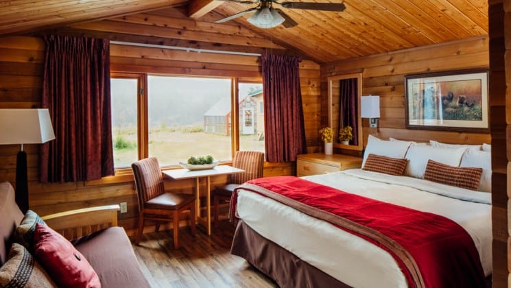 King bed, windowside table and two chairs, wooden detailing and futon in Superior Cabin at Denali Backcountry Lodge in Kantishna, Alaska