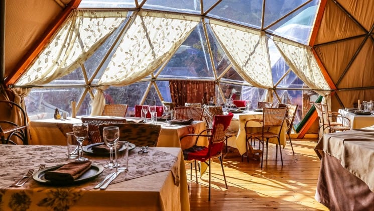 Light washes over the Dining Room Dome, where tables with elegant place settings are set up at EcoCamp in Patagonia, Chile
