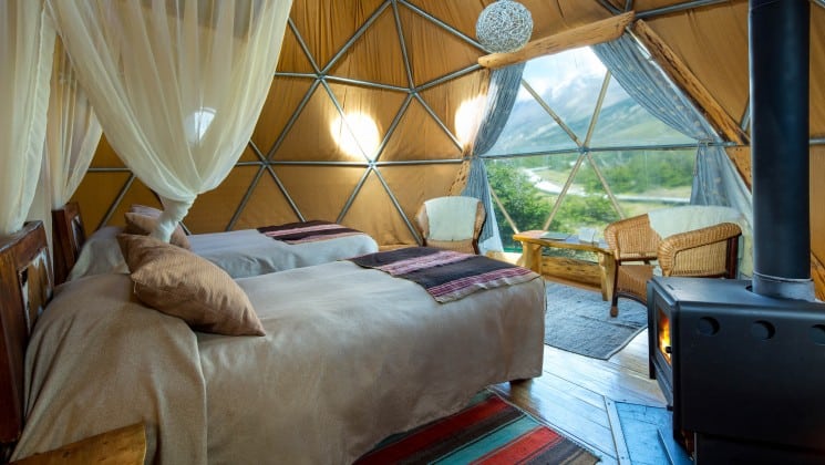 Two twin beds with small stove and curtains open for mountain views in Suite Dome at EcoCamp in Patagonia, Chile