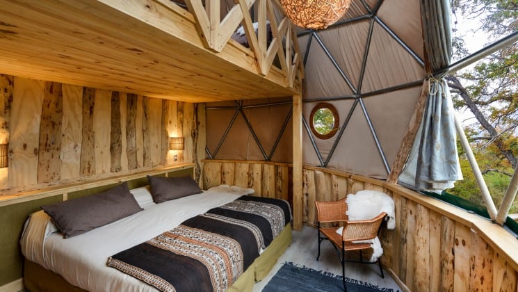 Downstairs bed near large windows with lofted area in Suite Dome at EcoCamp in Patagonia, Chile
