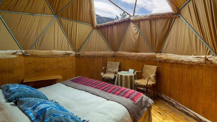 Dome with bed, two chairs, table, bench and skylight with mountain views at EcoCamp in Patagonia, Chile