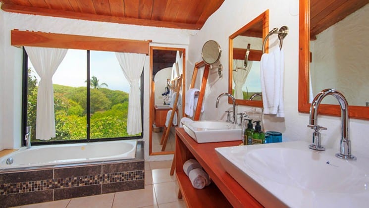 Bathroom with tub, twin sinks and mirrors, windows at Galapagos Habitat Eco Luxury Hotel on the Galapagos Island of Santa Cruz