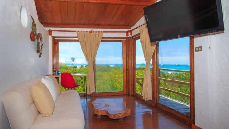 Couch, coffee table, TV, side table with stool, sliding door to balcony with ocean views at Galapagos Habitat Eco Luxury Hotel on the Galapagos Island of Santa Cruz