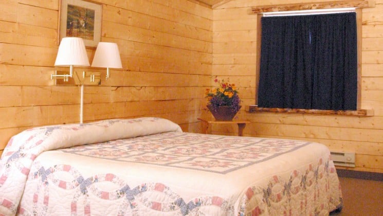 One queen-sized bed with a floral duvet, reading lights, Alaskan white spruce walls inside a handicap accessible cabin at the Kantishna Roadhouse, a lodge in Denali National Park