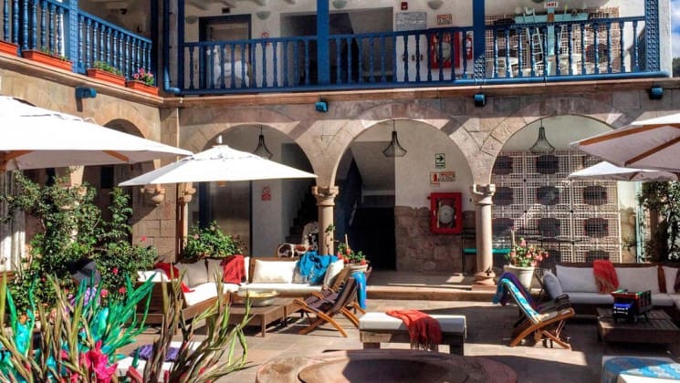 Sunny, open air courtyard with lounges, shade umbrellas, plants and stairs to upper level at El Mercado Tunqui in Cusco, Peru