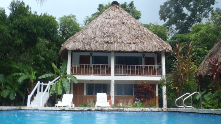 The main building at the Tikal Inn, a bungalow with a thatched roof, swimming pool, and lounge chairs.