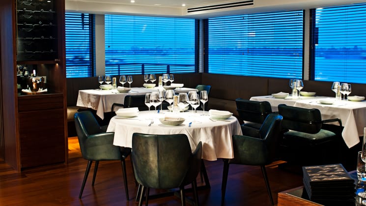 Aqua Mekong Dining Room with white table clothes, black chairs and large windows.
