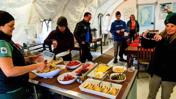 A woman is serving dinner with fresh ingredients to guests, buffet-style, at Base Camp Greenland in Sermilik Fjord