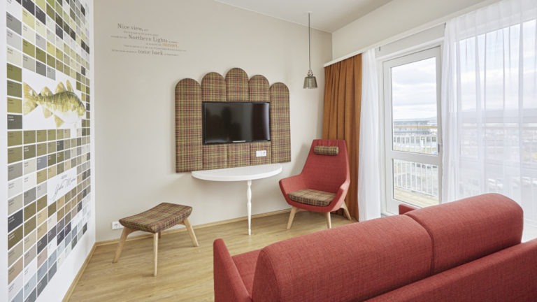A different angle of the contemporary junior suite, with a flat-screen tv, couch, chairs, and large windows overlooking the harbor, at the the Icelandair Reykjavik Marina Hotel