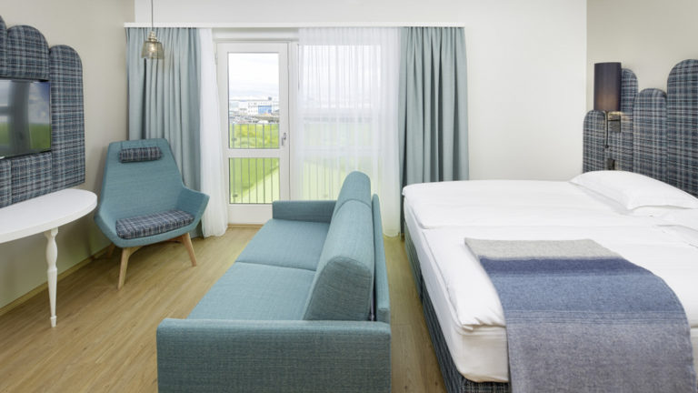 The contemporary junior suite, designed with maritime hues of blue, has a king-sized bed, couch, and television, at the the Icelandair Reykjavik Marina Hotel