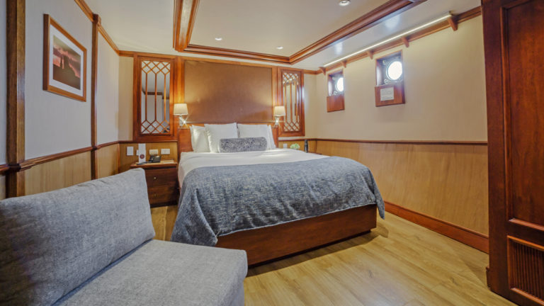 Grace stateroom with queen bed, chair and portholes.