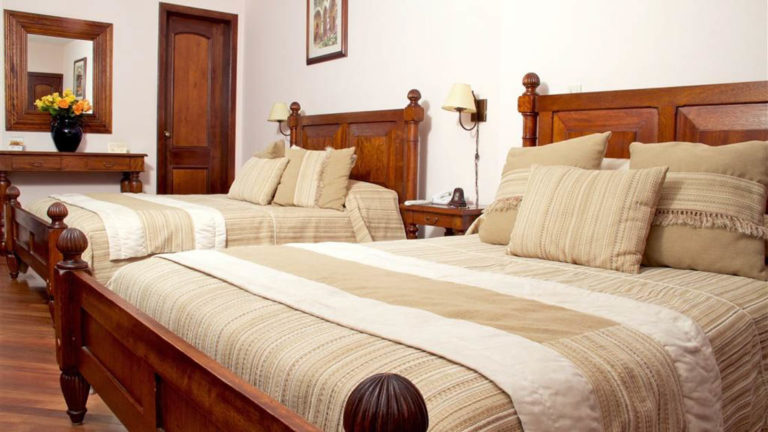 A room with two large beds and wooden furnishings offers guests a relaxing place to stay at the charming Hotel Patio Andaluz in Quito, Ecuador