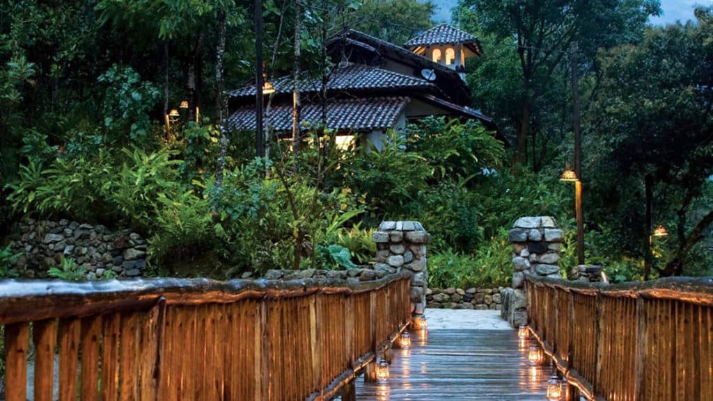A wooden bridge and railing lead to a stone pathway that winds through 12 acres of lush vegetation with rich biodiversity at the Inkaterra Machu Picchu Pueblo Hotel, a National Geographic Unique Lodge of the World.