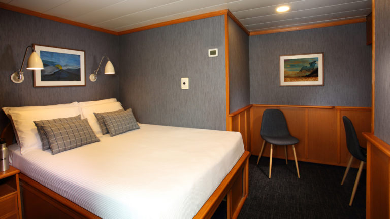 Isabela II stateroom with double bed, chairs, nightstands and reading lights.