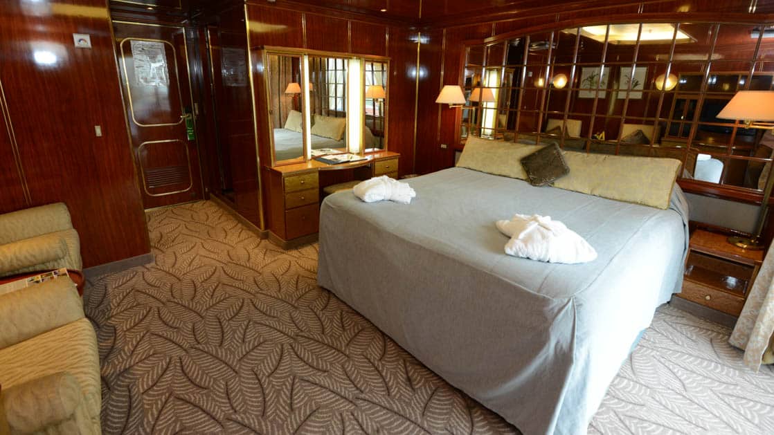 Island Sky Veranda suite with queen bed, nightstands, reading light, desk, sliding glass door to balcony.