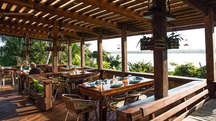 Open-air dining with tables and chairs overlooking the clear waters of the New River Lagoon at the Lamanai Outpost, a sustainable eco jungle lodge in Belize