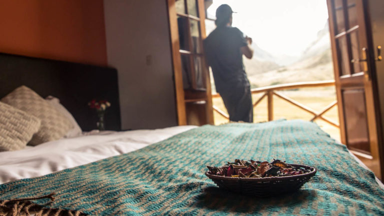 A person stands on the private balcony adjacent to a bedroom and sips a hot drink at the Salkantay Lodge and Adventure Resort, one of four hotels at the Mountain Lodges of Peru on the Inca Trail to Machu Picchu.
