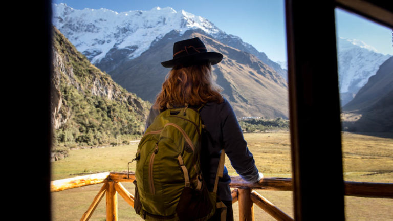 A woman stands on the porch ready to go hike into the snow-capped mountains in the distance, with a backpack, at the Salkantay Lodge and Adventure Resort, one of four hotels at the Mountain Lodges of Peru on the Inca Trail to Machu Picchu.