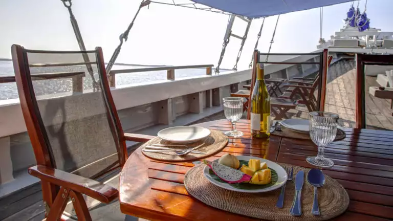 delicious food and a bottle of wine on a table on the deck of the ombak putih yacht on a sunny day