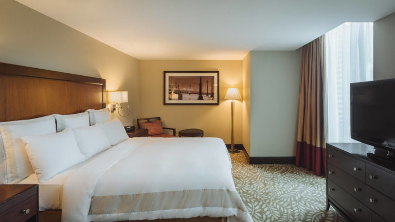 A king-sized bed with white linens, a television, and a private balcony at the Marriott Hotel in Panama City.