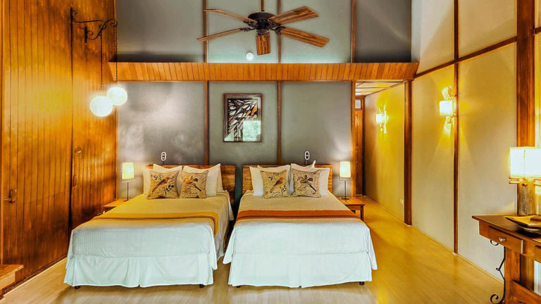 Two twin beds in a forest room with a ceiling fan and wood beams at the Monteverde Lodge, a sustainable, nature retreat on the edge of a well-known cloud forest in Costa Rica
