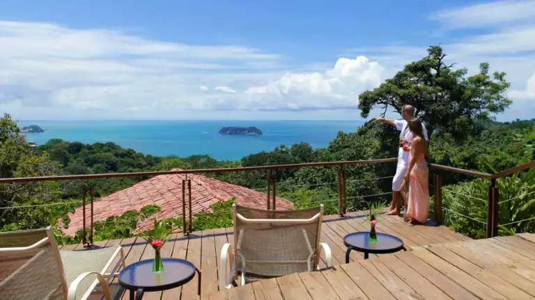 A deck with lounge chairs and small tables overlooks the red tiled roofs at Si Como No, a boutique resort, and the Pacific Coastline in Costa Rica