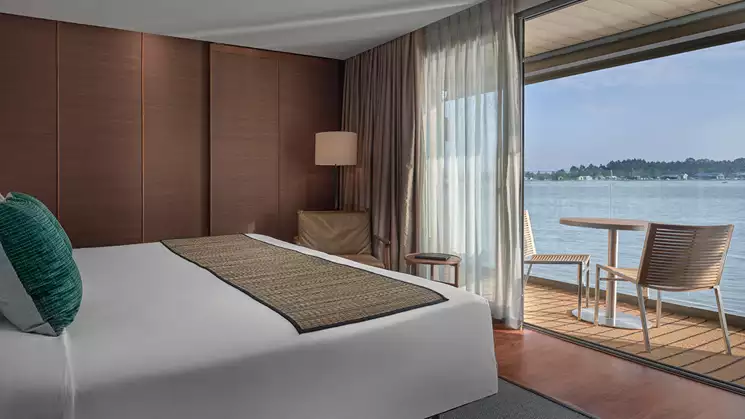 A beautiful suite on the first deck of the Aqua Mekong featuring a large bed with light linens and great views of the Mekong