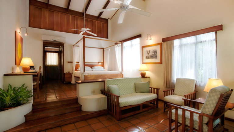 A superior suite at Hotel Capitán Suizo features a queen-sized bed with a canopy, sitting area, and large windows to enjoy jungle and beach views at Playa Tamarindo, Costa Rica