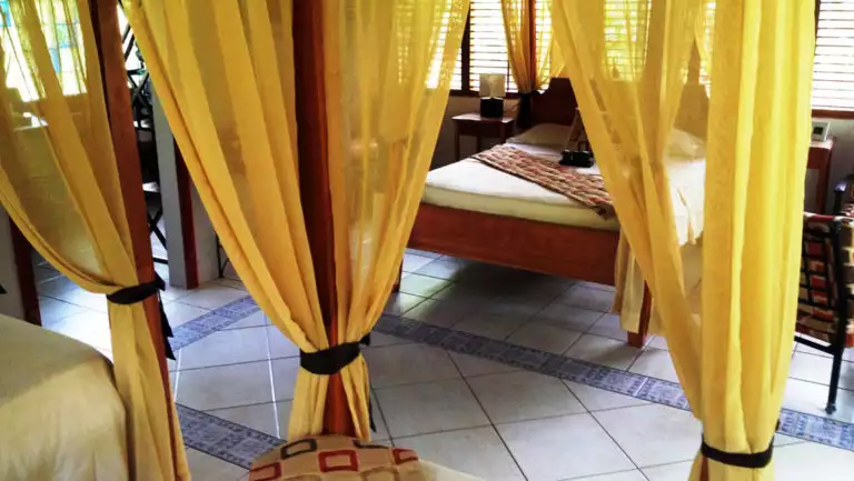 Four-post bed with yellow curtains and tile floor in a deluxe bungalow at Casa Corcovado Jungle Lodge in Costa Rica