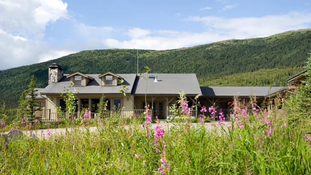 The North Face Lodge, set in the Alaskan wilderness next to a field of wildflowers and hills, is a traditional north-country inn located within Denali National Park