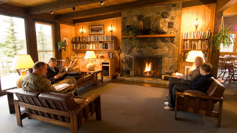 The lobby of the North Face Lodge, a wilderness accommodation in Alaska, with a wood-burning fireplace and comfortable couches. This is a hotel located within Denali National Park.
