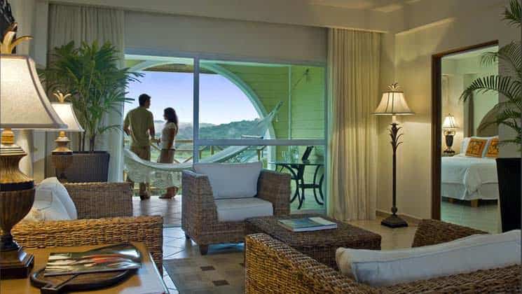 Couple stands on balcony with hammock, table and chairs, with living room with wicker coffee table and three chairs at Gamboa Rainforest Resort in Panama