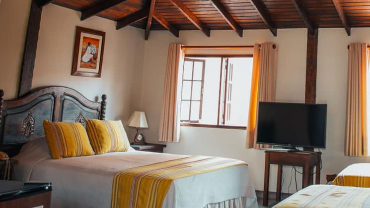 suite room with three beds with yellow and white theme and wooden beams on the ceiling at the hotel antigua miraflores in peru