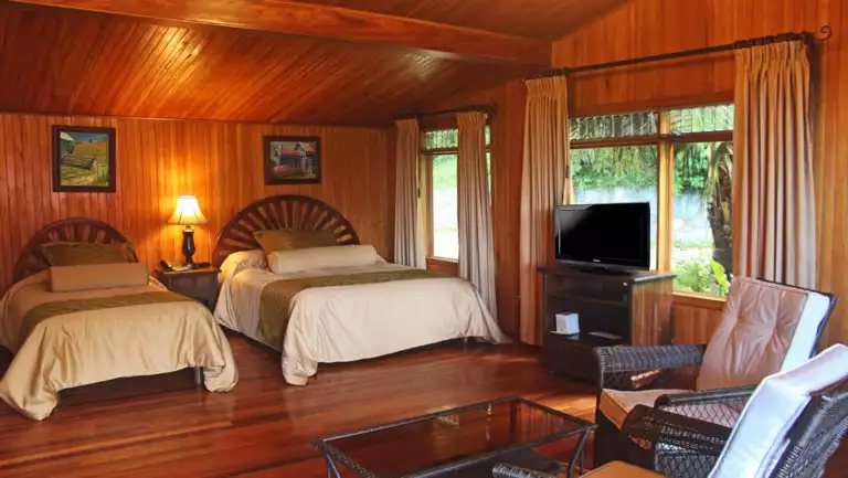 Interior of Standard Room with two beds, table and chairs, TV and windows at Hotel Fonda Vela in Monteverde, Costa Rica