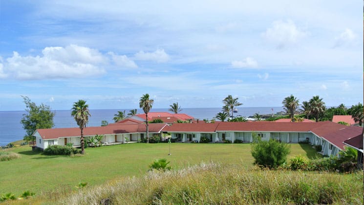 exterior view of hotel iorana easter island in chile with a large lawn around it, sunny skies above and the ocean in the distance