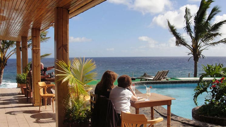 travelers relaxing outside by the pool looking at the ocean with a palm tree blowing in the wind at hotel iorana easter island in chile