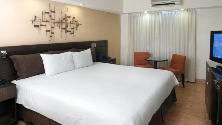 The Standard King Room with a large bed, white linens, and lighting at the four-star Hotel Presidente, in downtown San José, Costa Rica