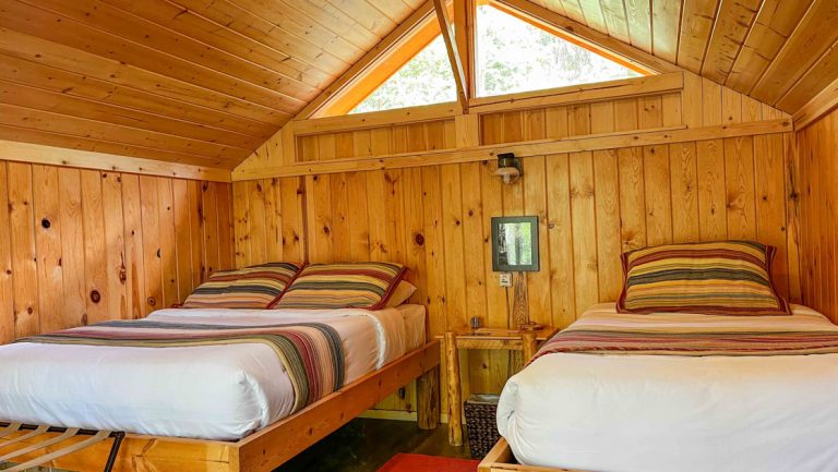 Interior of guest cabin at Kenai Backcountry Lodge with 1 double & 1 single bed, light wood bead board, skylights & table.