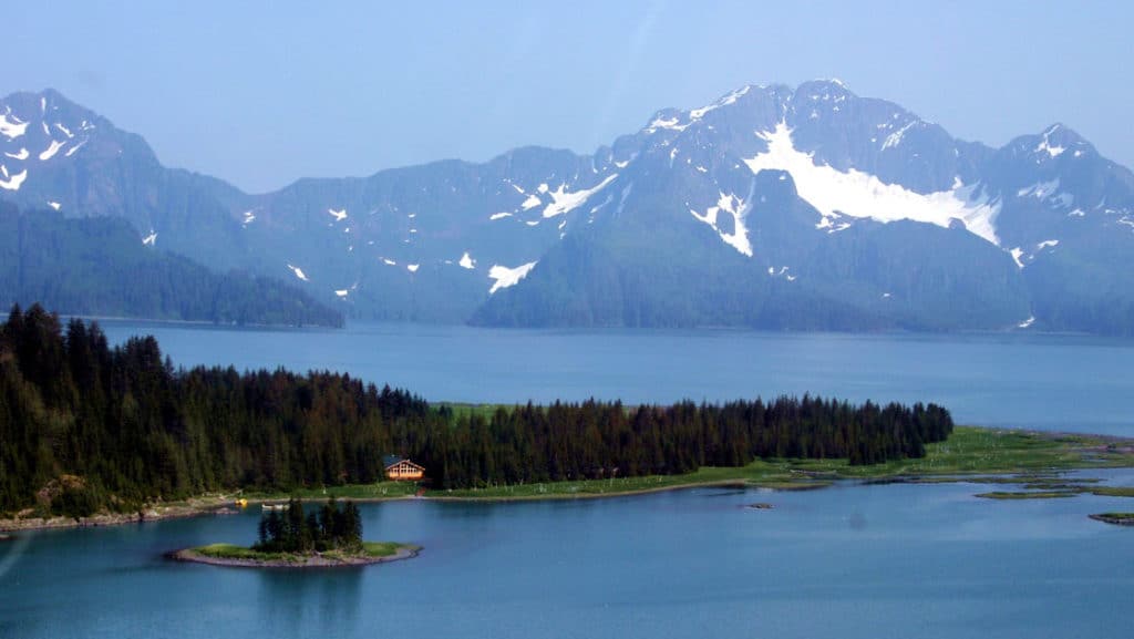 The Kenai Fjords Glacier Lodge is located within the 700,000-acre National Park. A view of the mountains, the Pedersen Glacier, a lake, and the forest where the hotel is nestled.