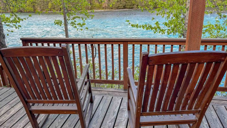 2 wood rocking chairts on deck at Kenai Riverside Lodge in Alaska overlooking rushing turquoise water & green forest.