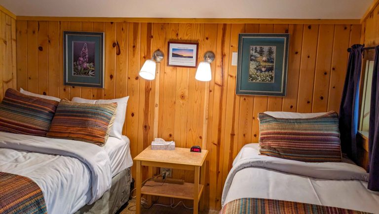 Double & twin bed made up in guest log cabin at Kenai Riverside Lodge, with reading lights, bedside table & small window.