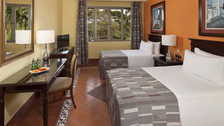 room with two crisp grey and white beds, table and chair and large window at melia hotel panama canal